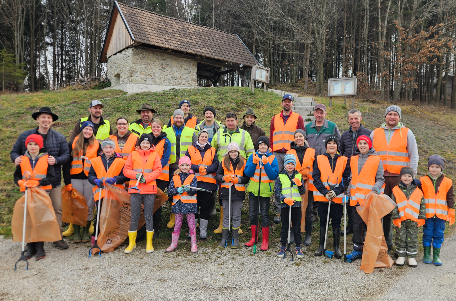 Gruppe von Erwachsenen und Kindern mit Warnwesten, Müllgreifern und Abfallsäcken