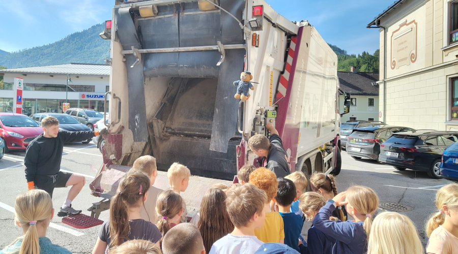 R&uuml;ckw&auml;rtige Ansicht einen M&uuml;llautos mit Kindergruppe davor.