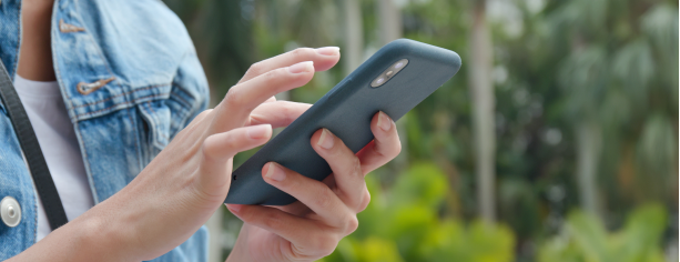 Person hält Smartphone in der Hand, im Hintergrund ist ein Garten