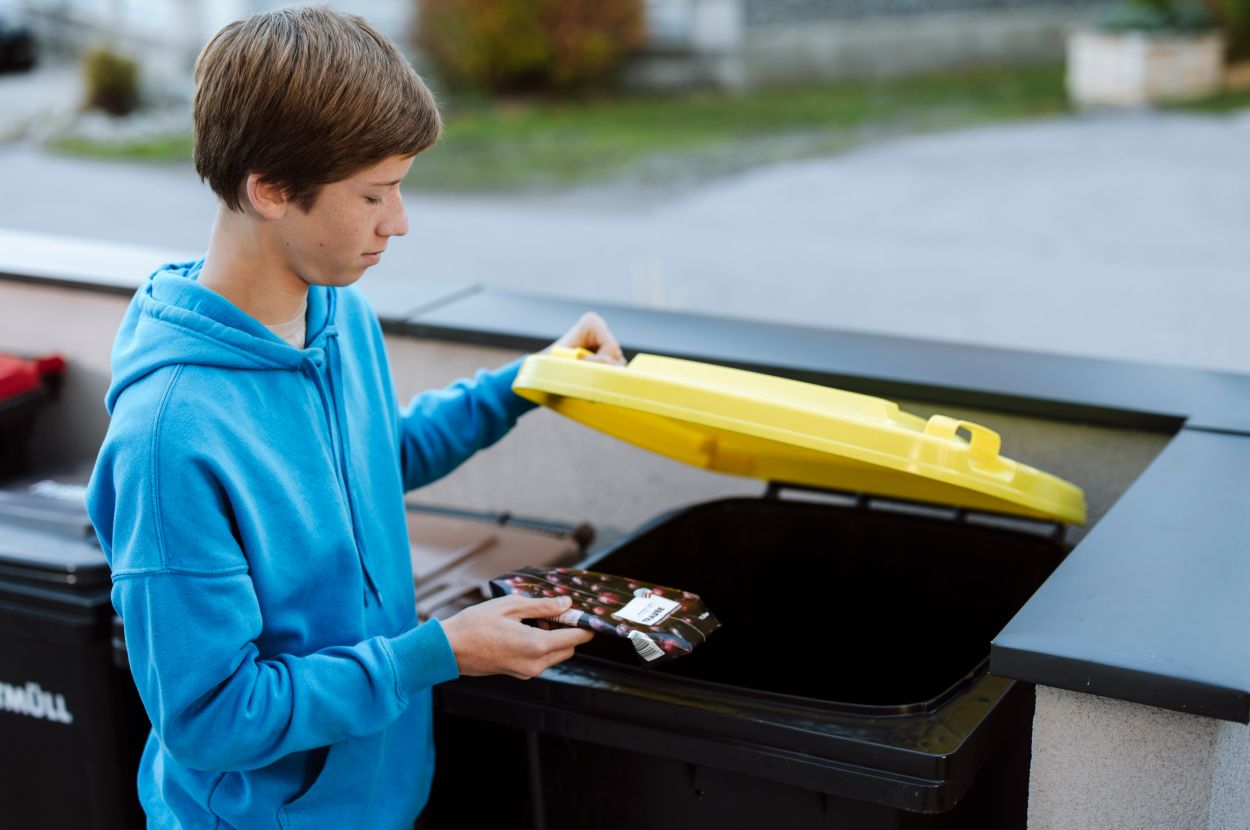 Teenager, der gerade eine Verpackung in die Gelbe Tonne gibt.
