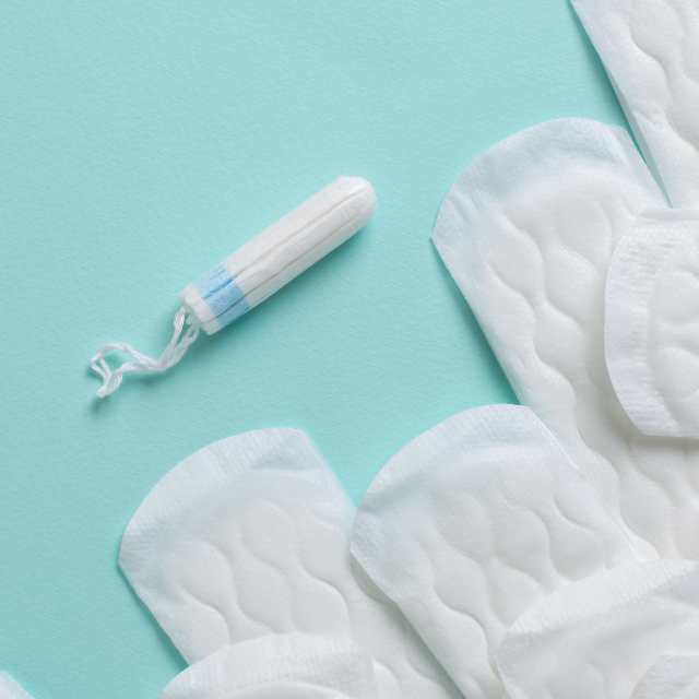 Ein Tampon und mehrere Slipeinlagen/Binden auf türkisem Hintergrund