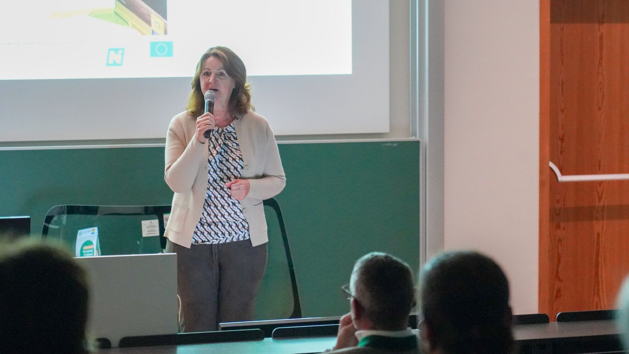 Frau mit Mikrofon steht vor einer Leinwand