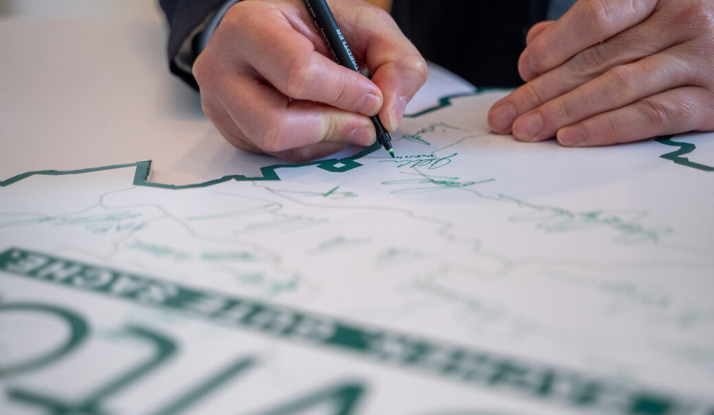 Auf dem Bild ist eine Niederösterreichkarte mit dem ReVital Logo zusehen sowie die diverse Unterschriften und eine Hand, die einen grünen Stift hält und unterschreibt.