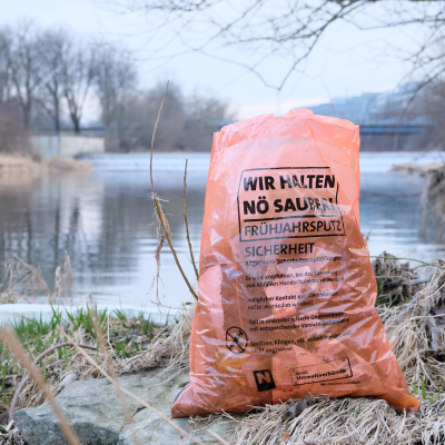 Ein gefüllter Müllsack vom Frühjahrsputz steht am Flussrand