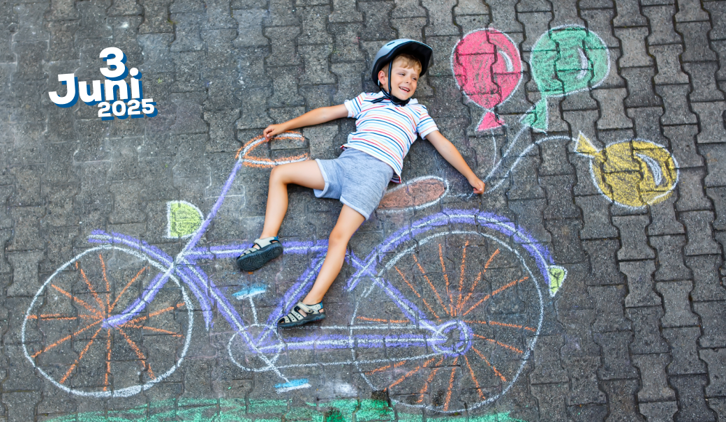 Das Foto zeigt ein Kind, das mit Fahrradhelm auf dem Kopf mit einem Grinsen auf dem Boden liegt - aus der Vogelperspektive - mit Straßenkreiden ist ein Fahrrad aufgezeichnet und es sieht aus, als ob das Kind drei Luftballons, die ebenfalls mit Straßenkreiden aufgezeichnet worden sind, in der Hand hält.
