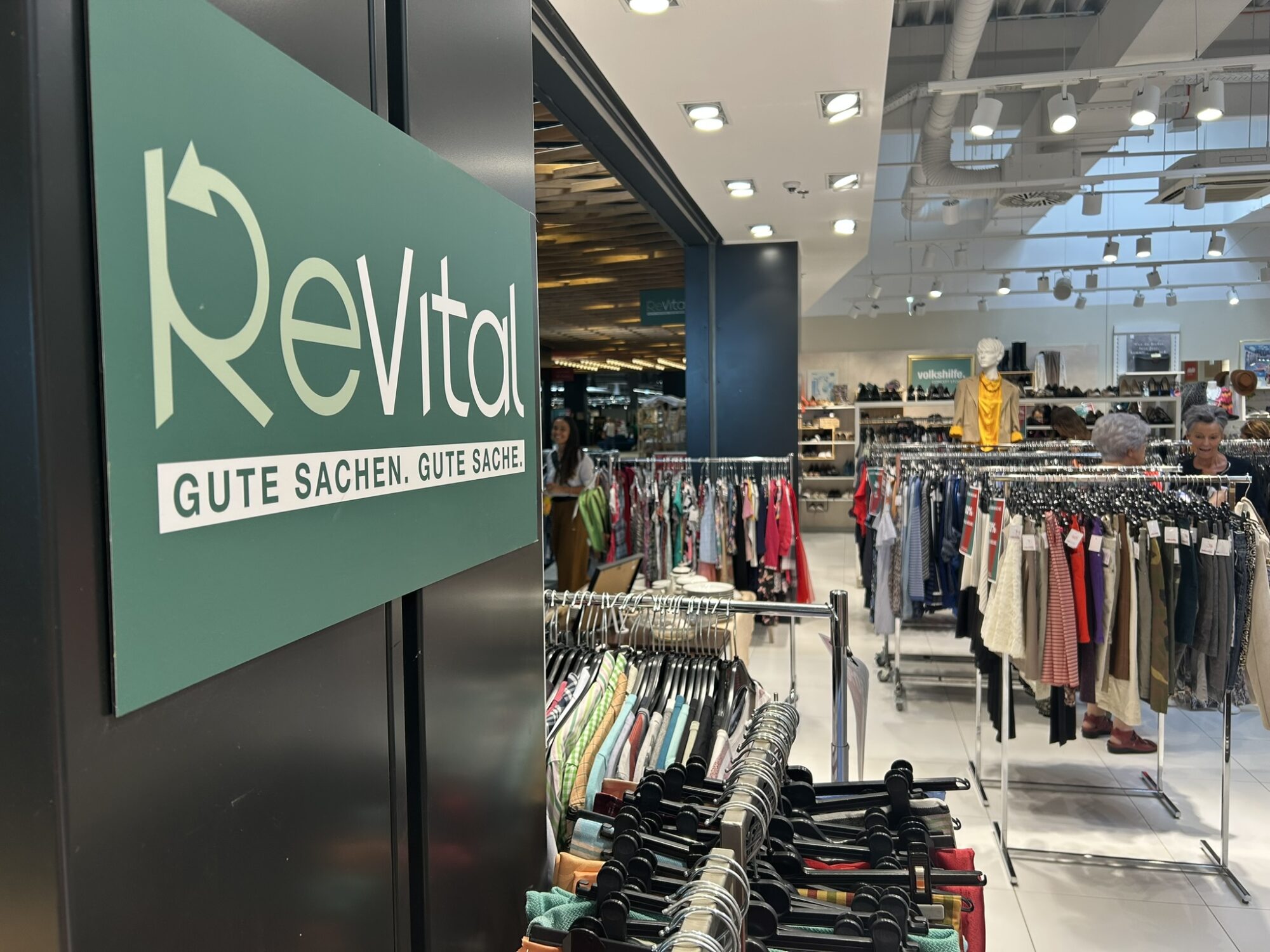 Werbeschild ReVital, im Hintergrund Warenkaufhaus mit Kleidung