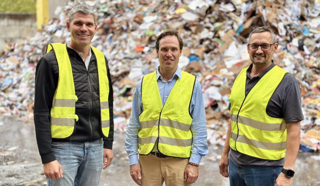 Bernhard Ebenführer, Christoph Merkens und Thomas Prenner stehen in Warnwesten vor einer großen Menge Altpapier