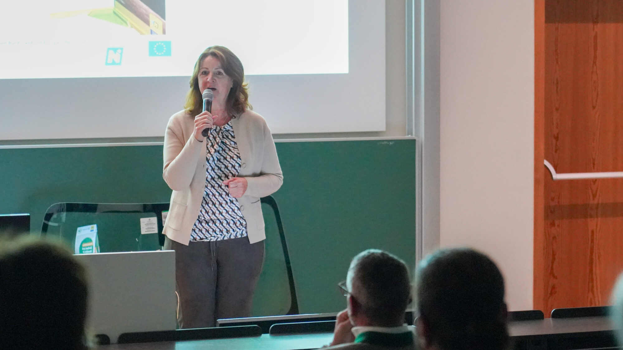 Frau mit Mikrofon steht vor einer Leinwand
