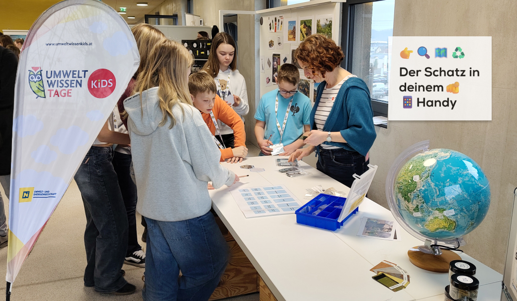 Jugendliche stehen interessiert an einem Tisch; im Vordergrund ist ein Globus und links im Bild eine Beachflag von Umwelt.Wissen